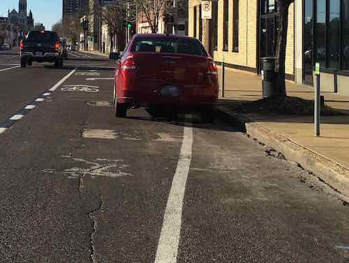 This Ford Escort is parked at a numbered spot and behind the 'no parking to corner sign. It's also blocking the right turn lane. WB Olive just East of Compton